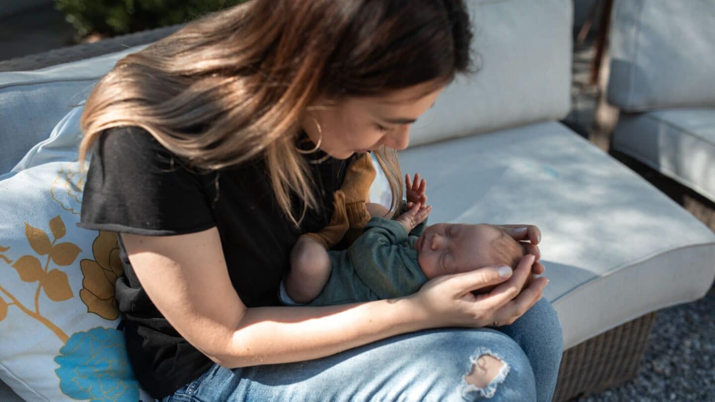 new mom holding newborn baby's head in her hands - causes of mommy thumb