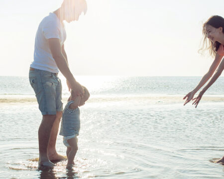 parents playing with baby in the ocean Motherly