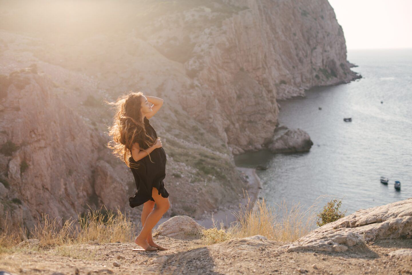 traveling during pregnancy, pregnant woman stands on lookout point with water and mountains in background