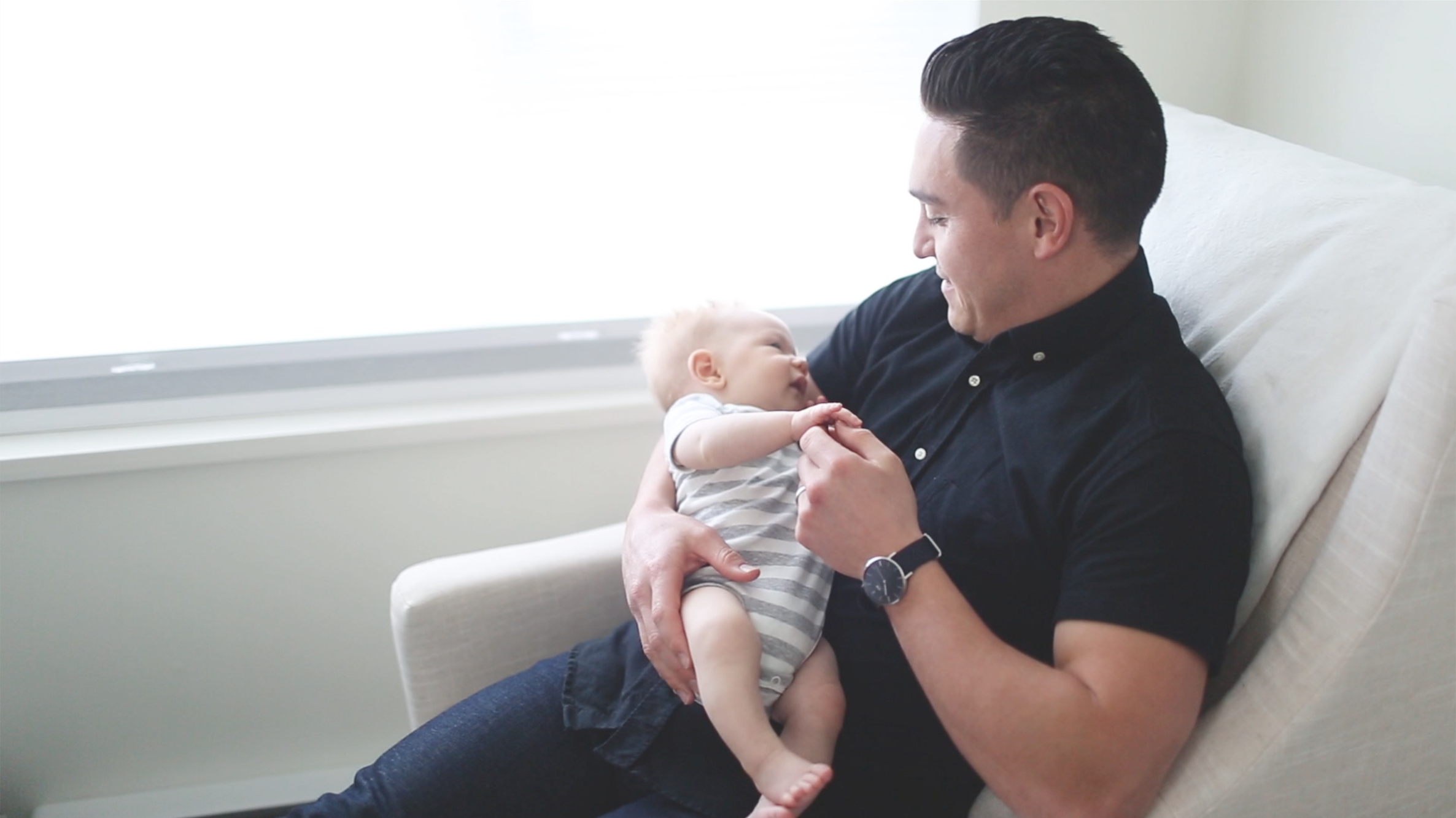 father holding baby sitting on sofa- dads are not babysitters