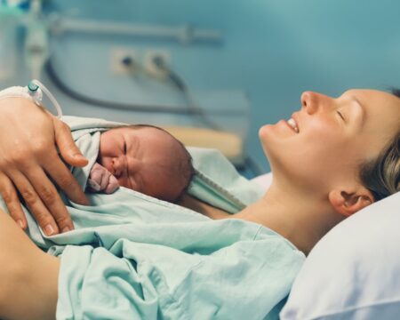 mother holding newborn baby in hospital bed and smiling possibly after using laughing gas for labor Motherly