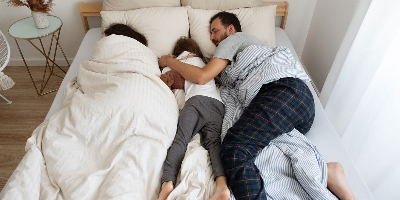 mom dad and child sleeping in one bed together - sleep needs by age