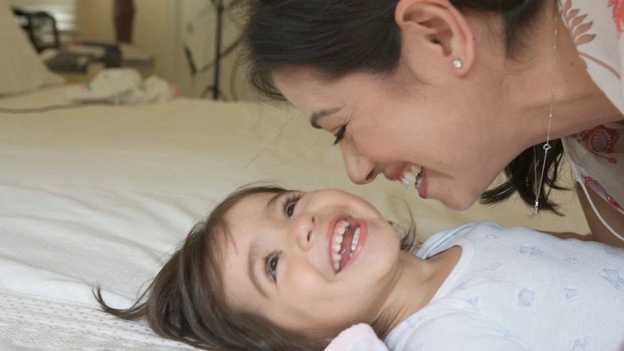 mom giggling with daughter laying on a bed