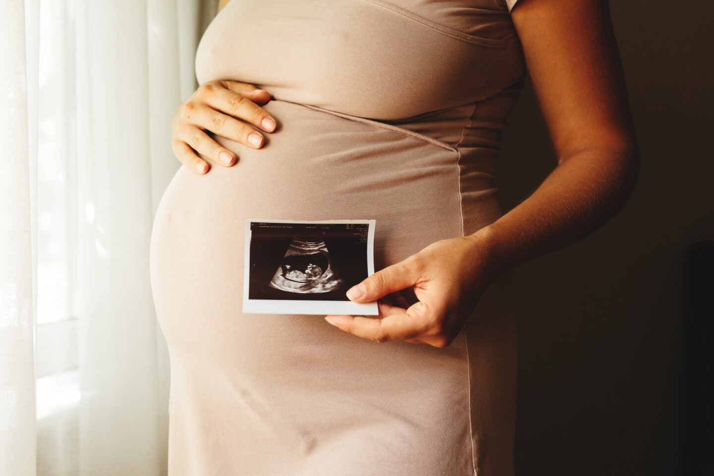 woman cradling her stomach and showing a sonogram photo