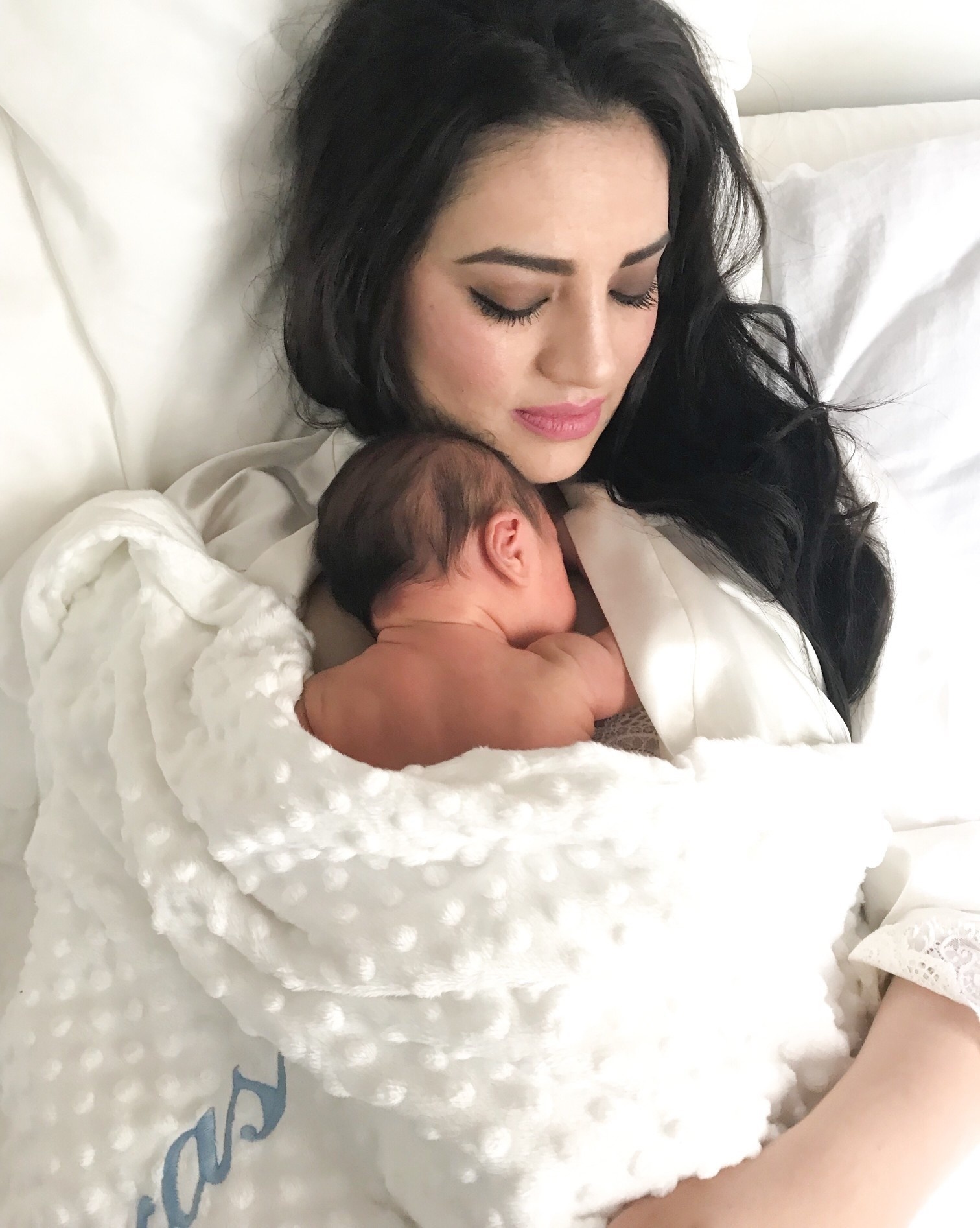 mom snuggling with baby on the bed wrapped in a blanket- motherhood is lonely