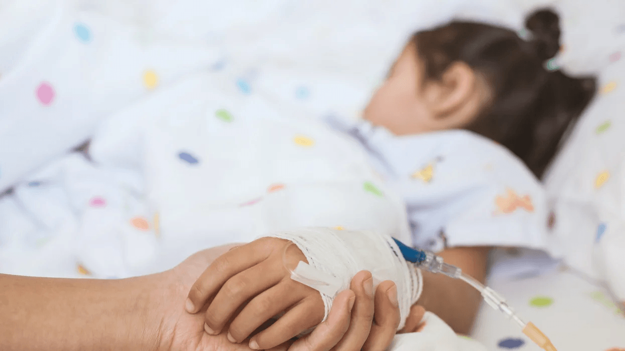 person holding child's hand in a hospital bed