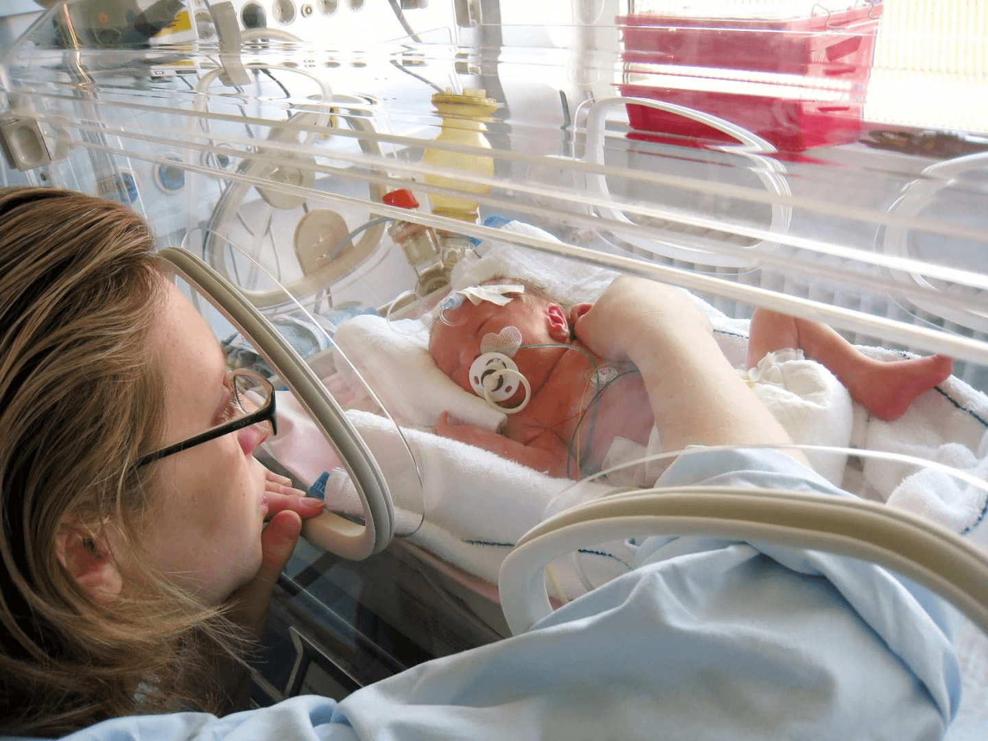 mom gently touching a baby in a NICU bed