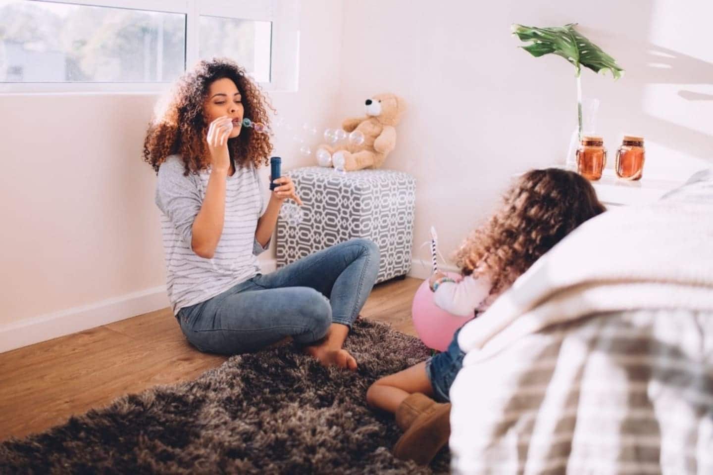 mom sitting on the floor blowing bubbles with daughter