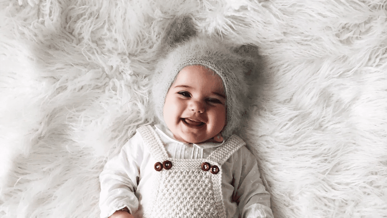 baby wearing a hat, laying on a fuzzy blanket, and smiling because its parents use montessori from birth