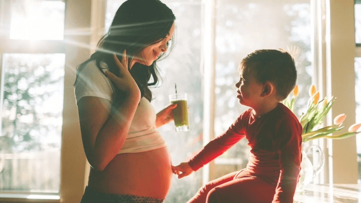 toddler touching prengnant moms belly while she drinks a smoothie