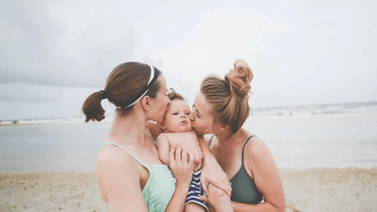 two women kissing toddler on the cheek