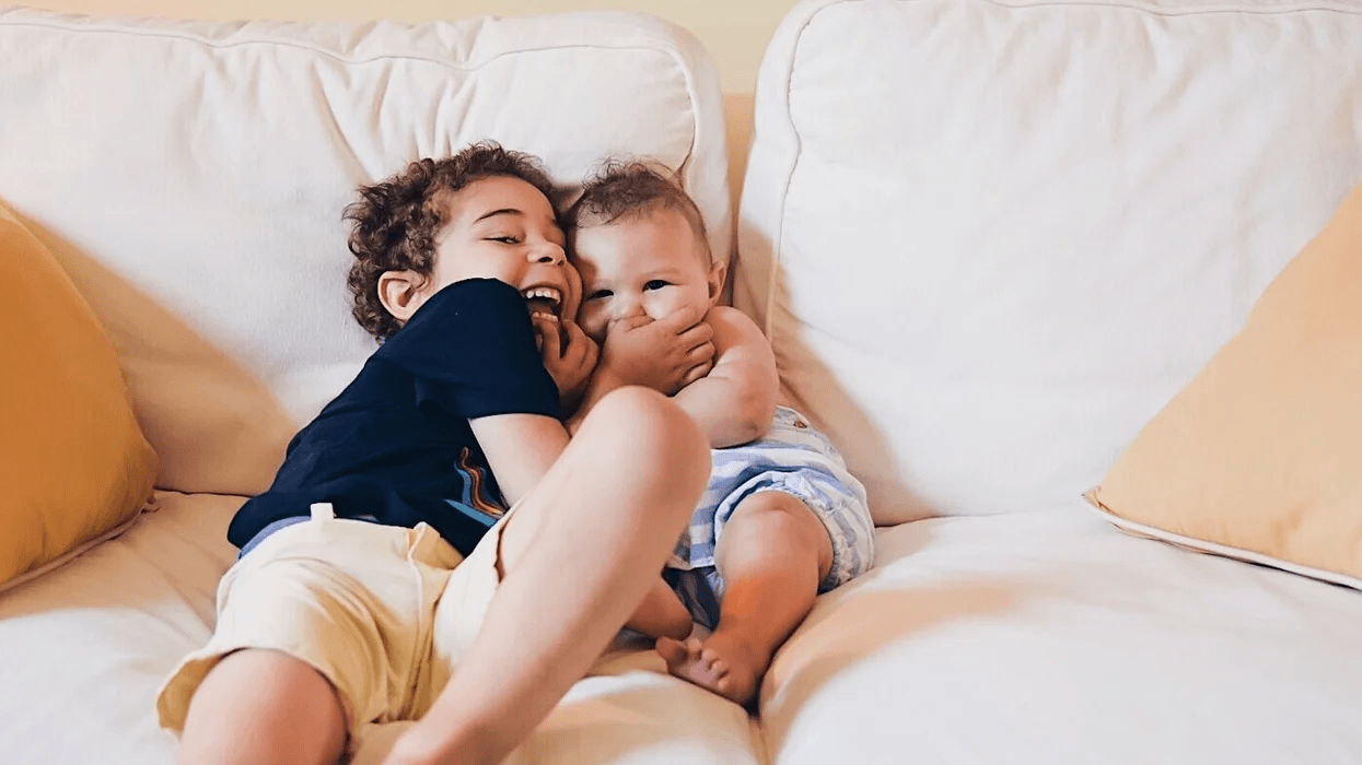 toddler and baby siblings hugging on the couch