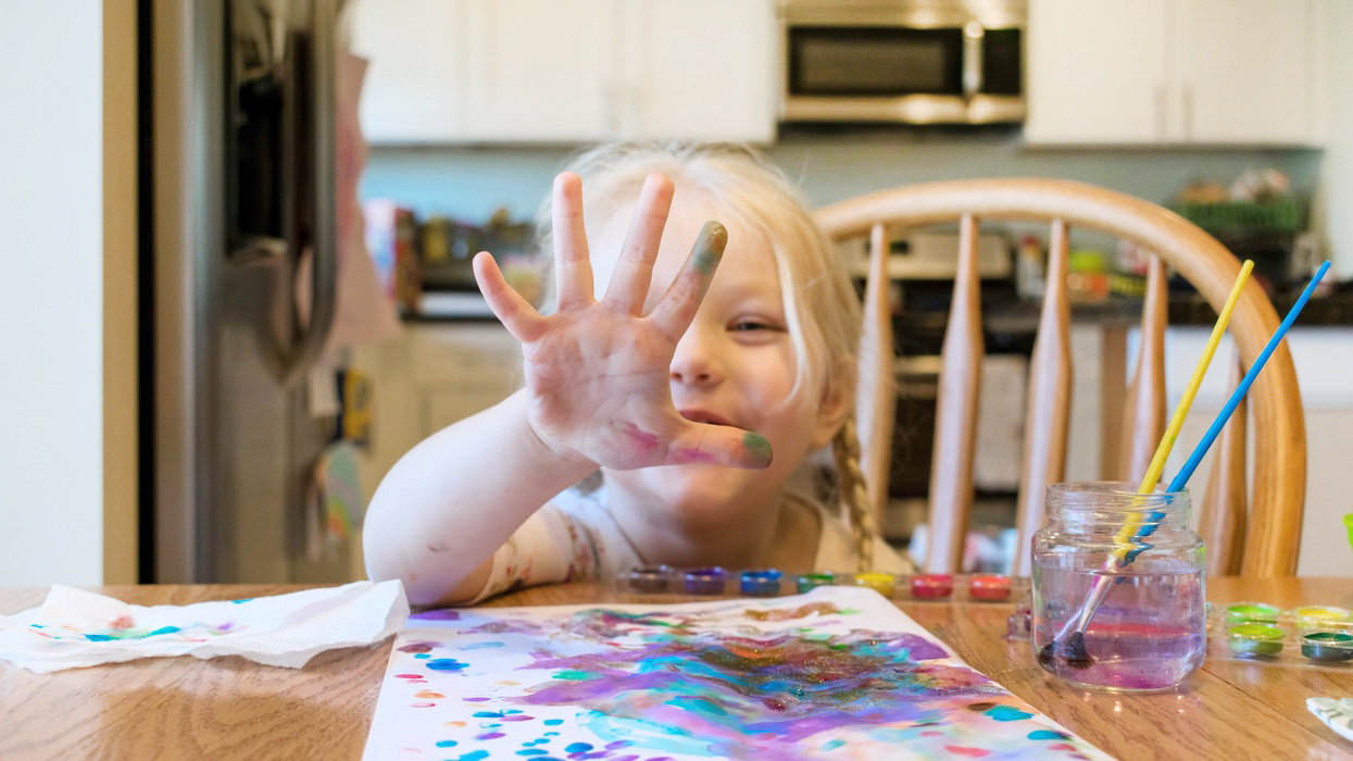 child holding up hand after finger painting, one of our favorite messy play activities