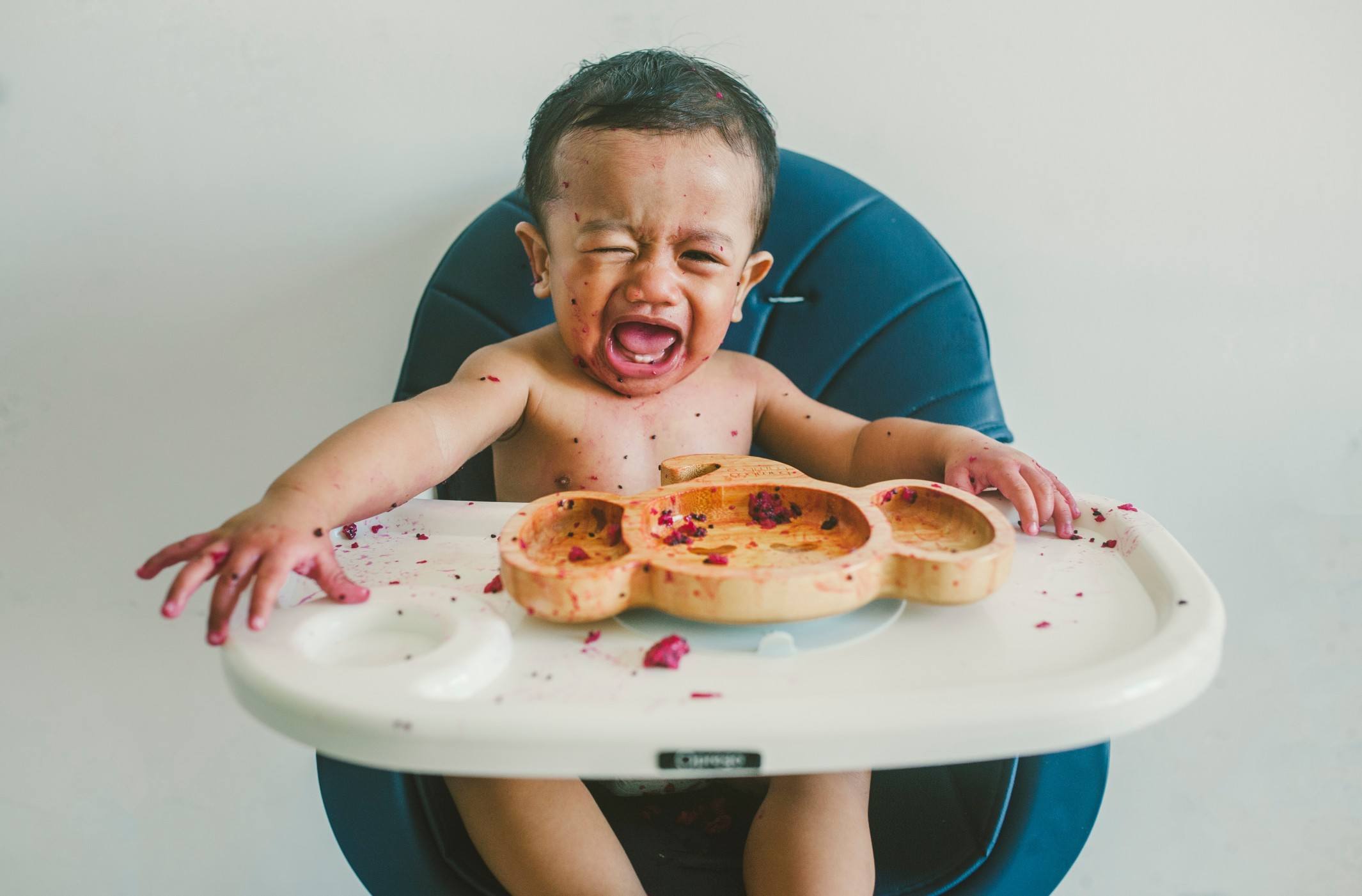 little boy crying while eating in a high chair