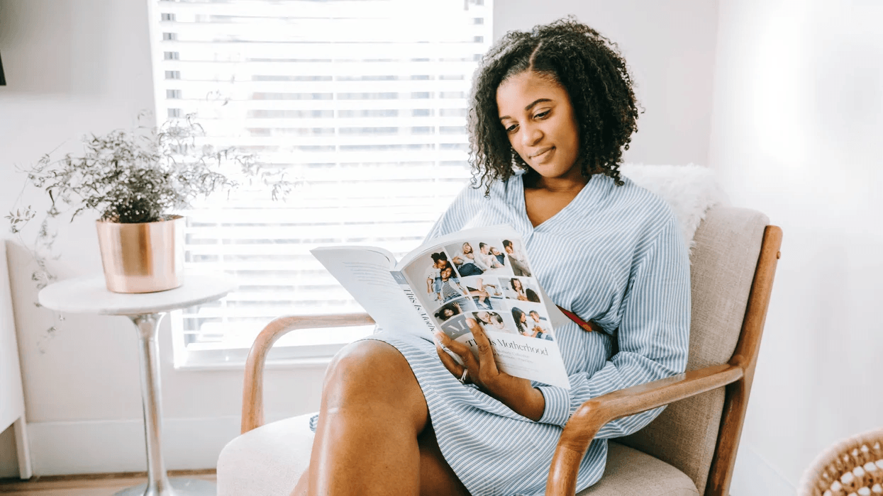 woman sitting on a chair reading this is motherhood book