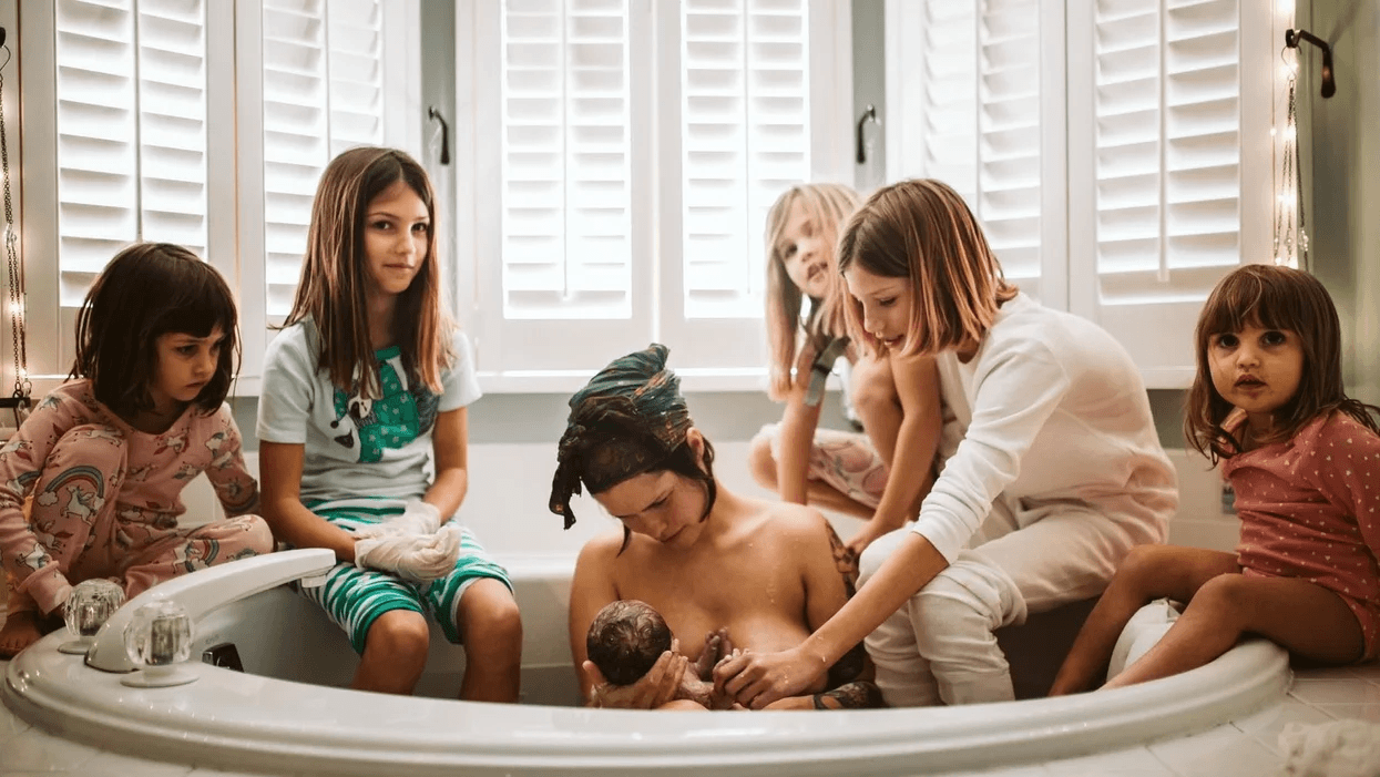 mom holding a newborn after a homebirth surrounded by her 5 kids