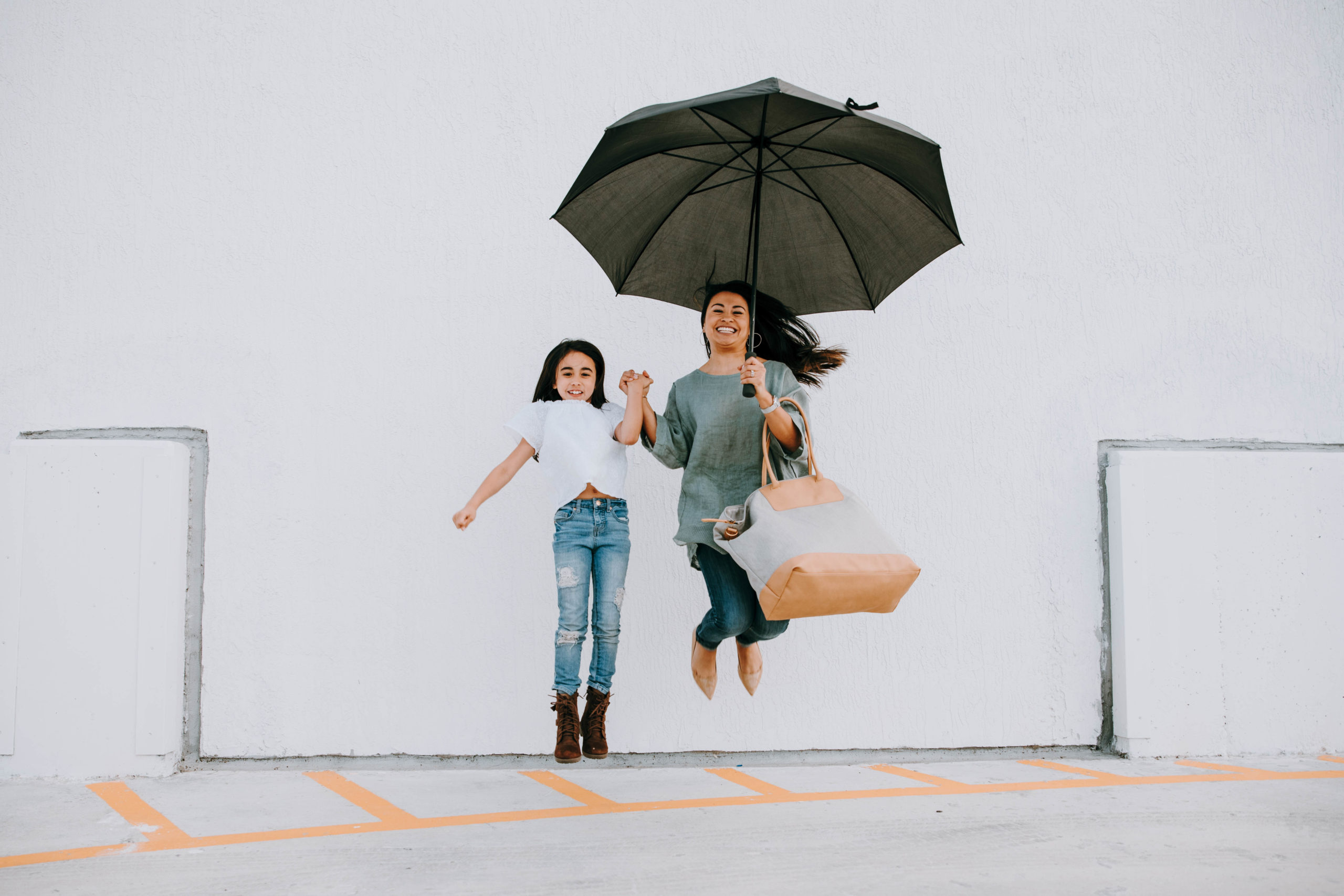 mom and daughter jumping and holding an umbrella