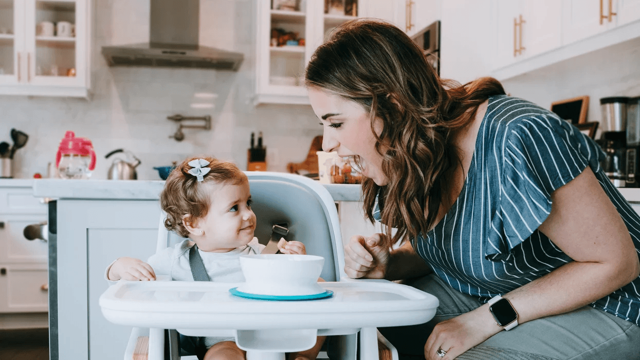 mom encouraging toddler eating in a high chair