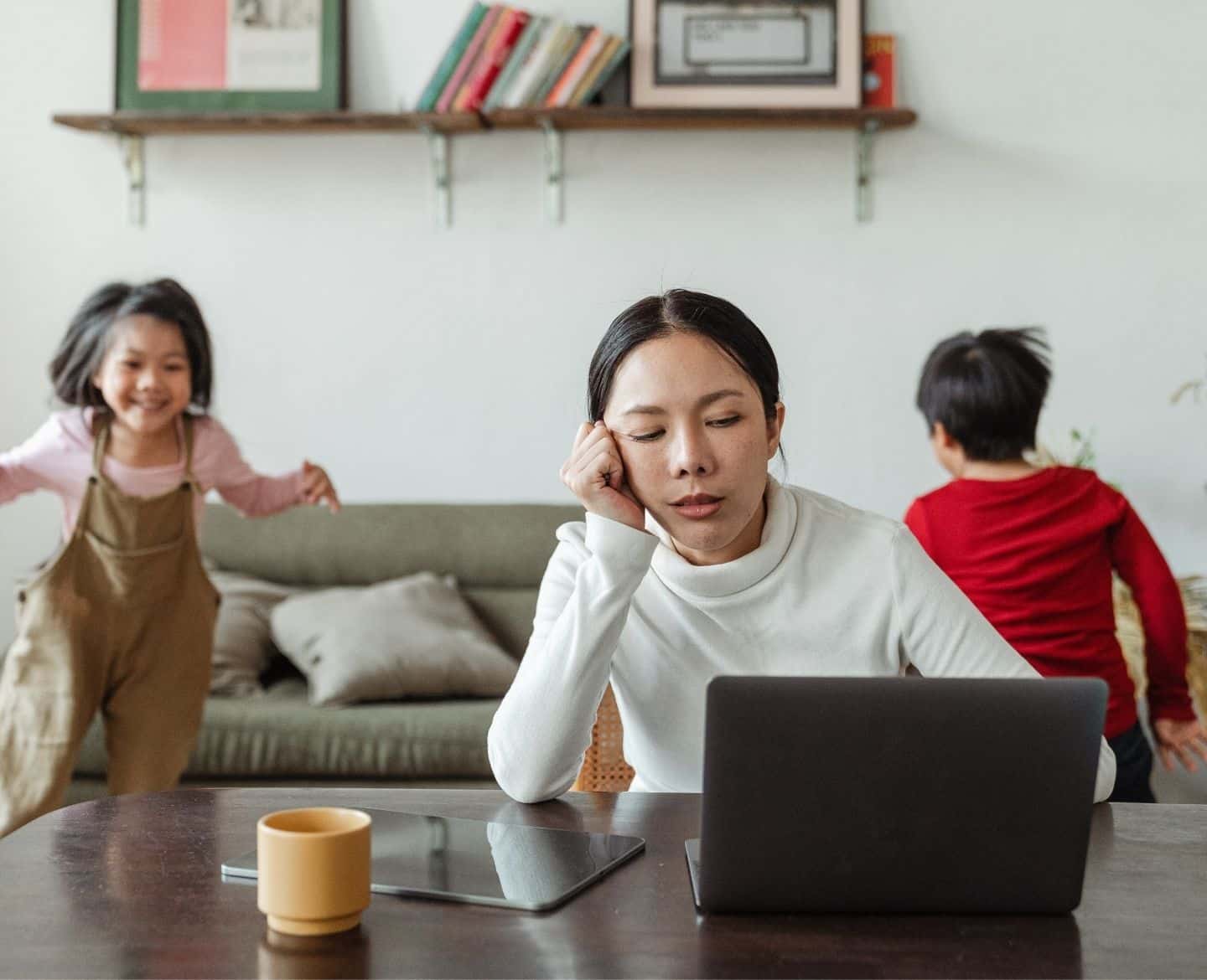 annoyed mama on a computer while kids play behind her