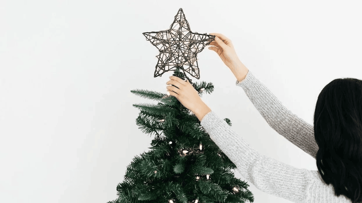 woman putting star on a Christmas tree- is it too early to decorate for christmas