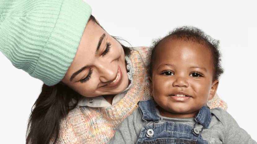 mom wearing a beanie holding a baby in overalls