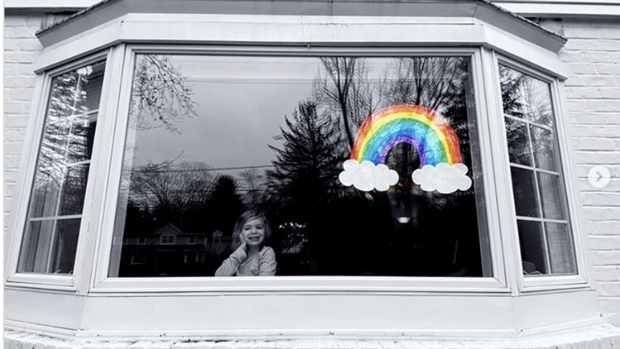 little girl looking out a window with a rainbow drawing on it