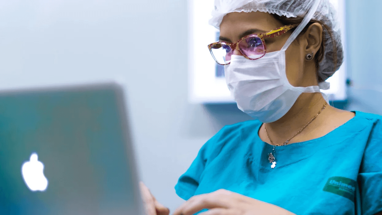 nurse wearing a mask and glasses working on a computer