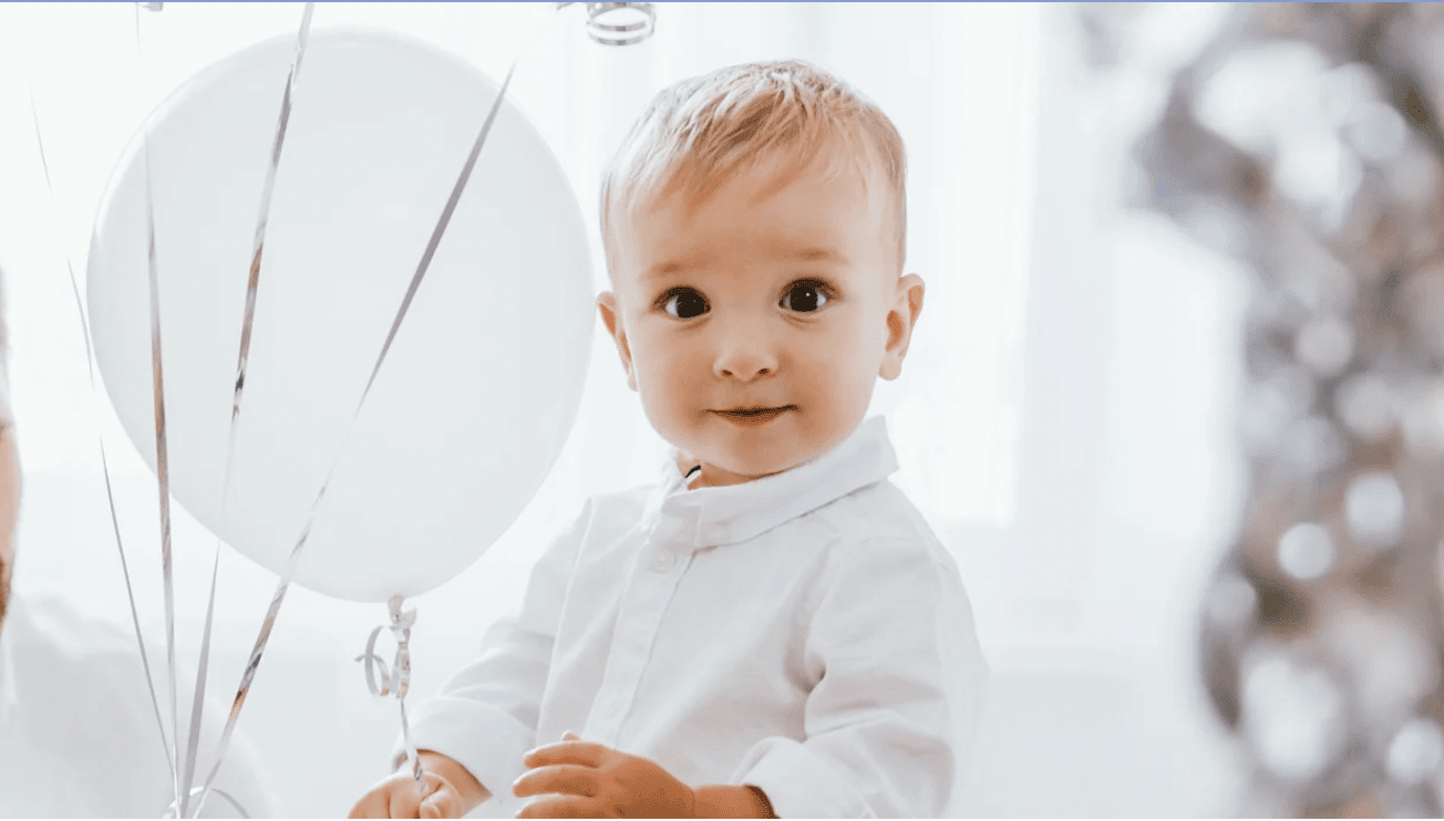 little boy looking at the camera with white balloons behind him