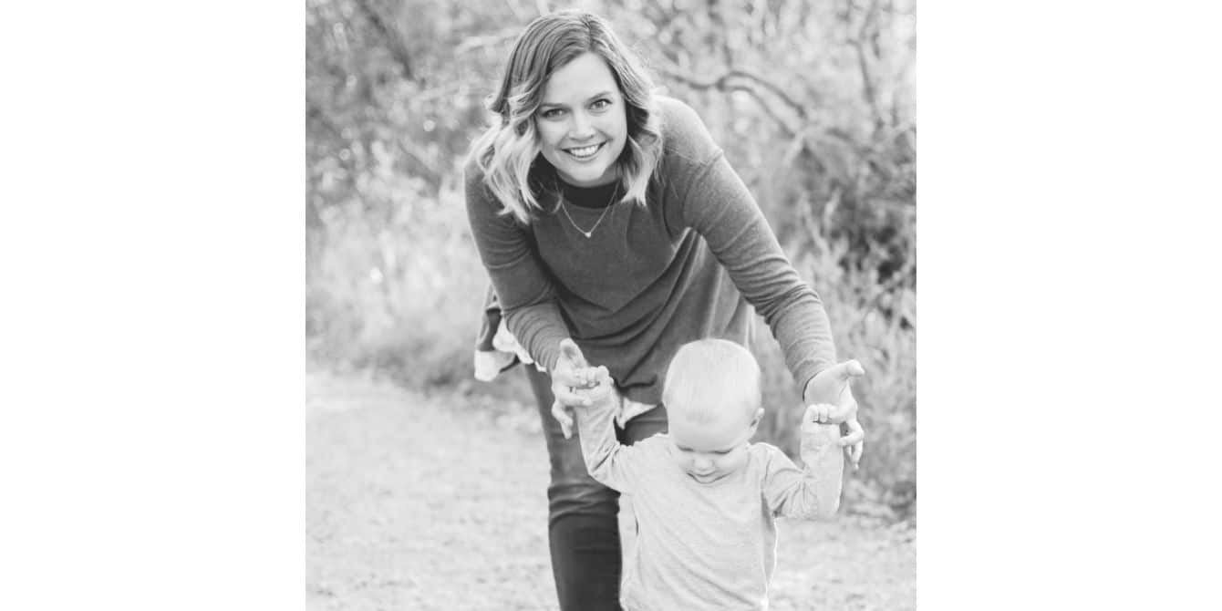 woman smiling for the camera and helping her baby to walk