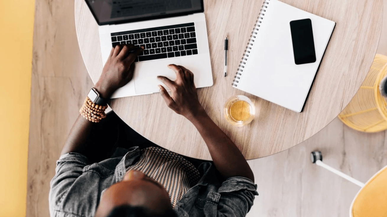 aerial shot of woman working on a laptop on a desk with coffee and a notebook