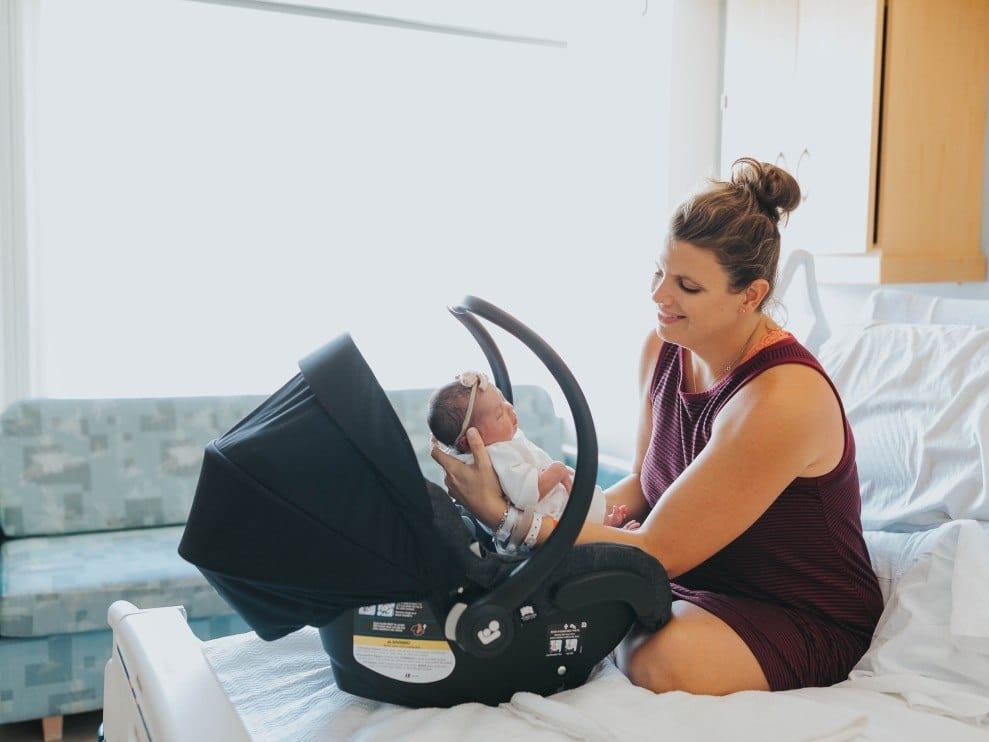 woman sitting in a hospital bed putting baby in a car seat