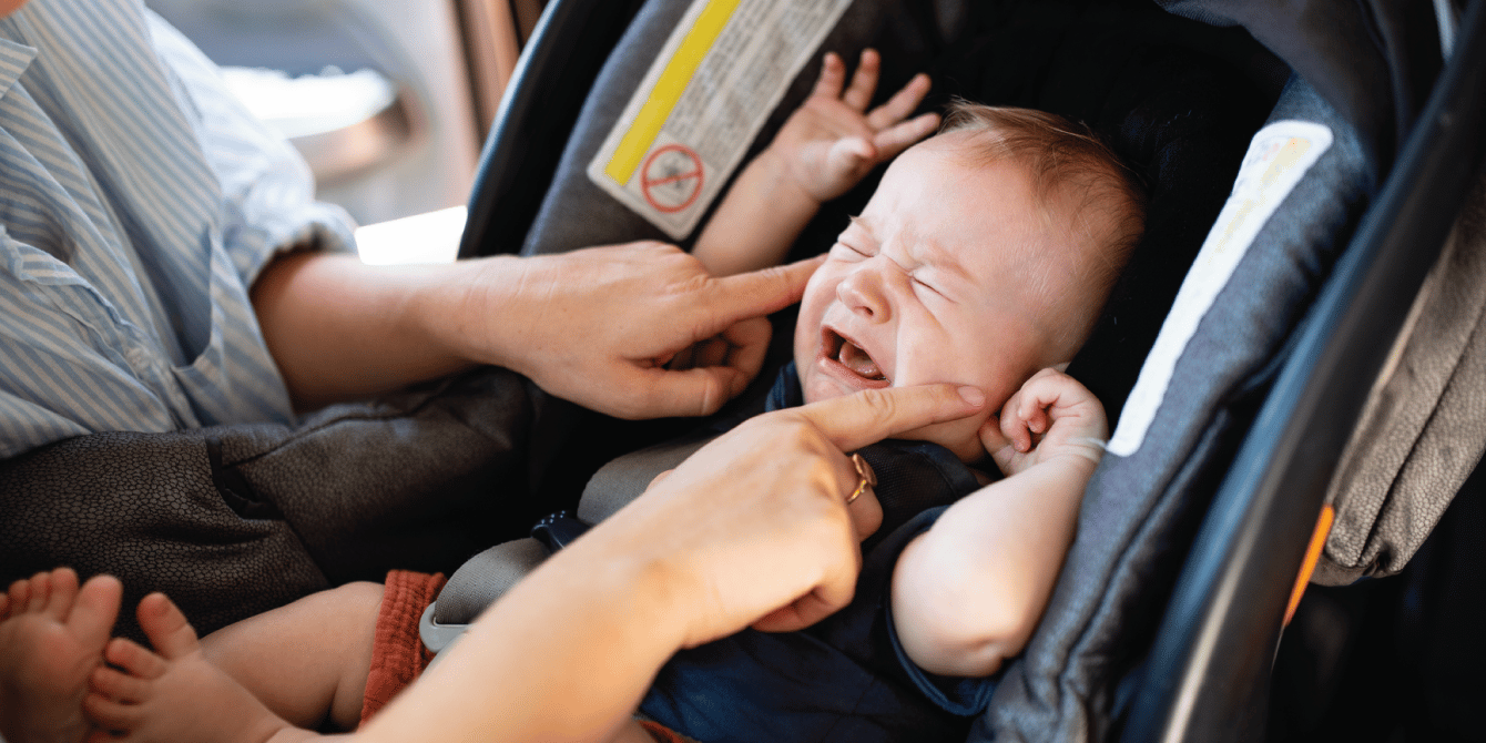 mom trying to comfort her baby as it cries in a car seat