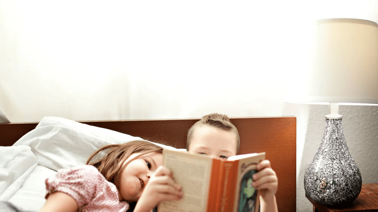 two kids reading a book together in bed