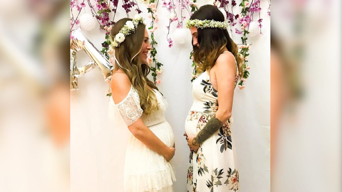 two friends showing their baby bumps wearing white dresses and floral headbands