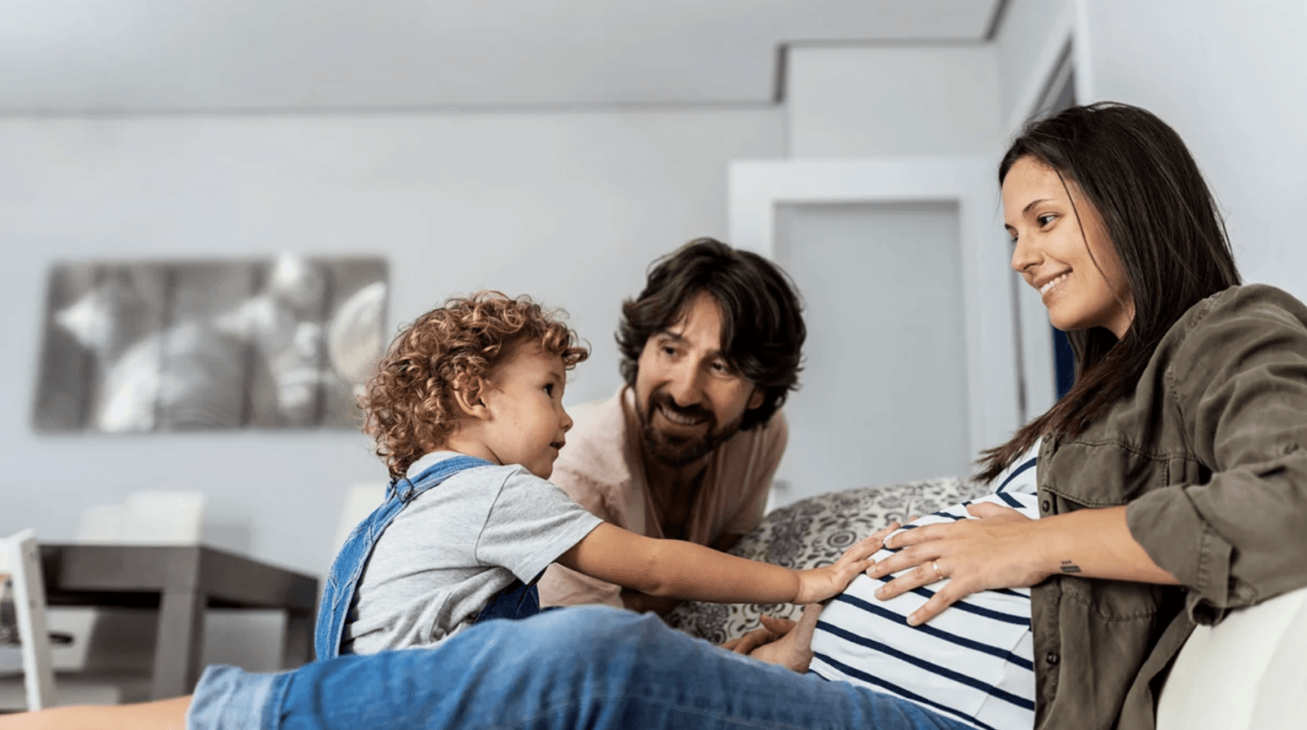 toddler touching pregnant moms belly while dad watches