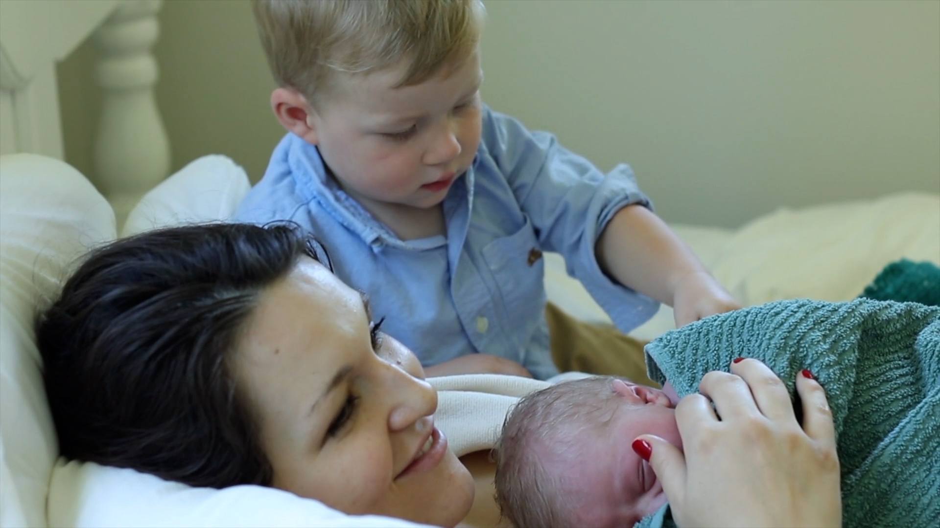mom holding newborn son while older son stands behind her