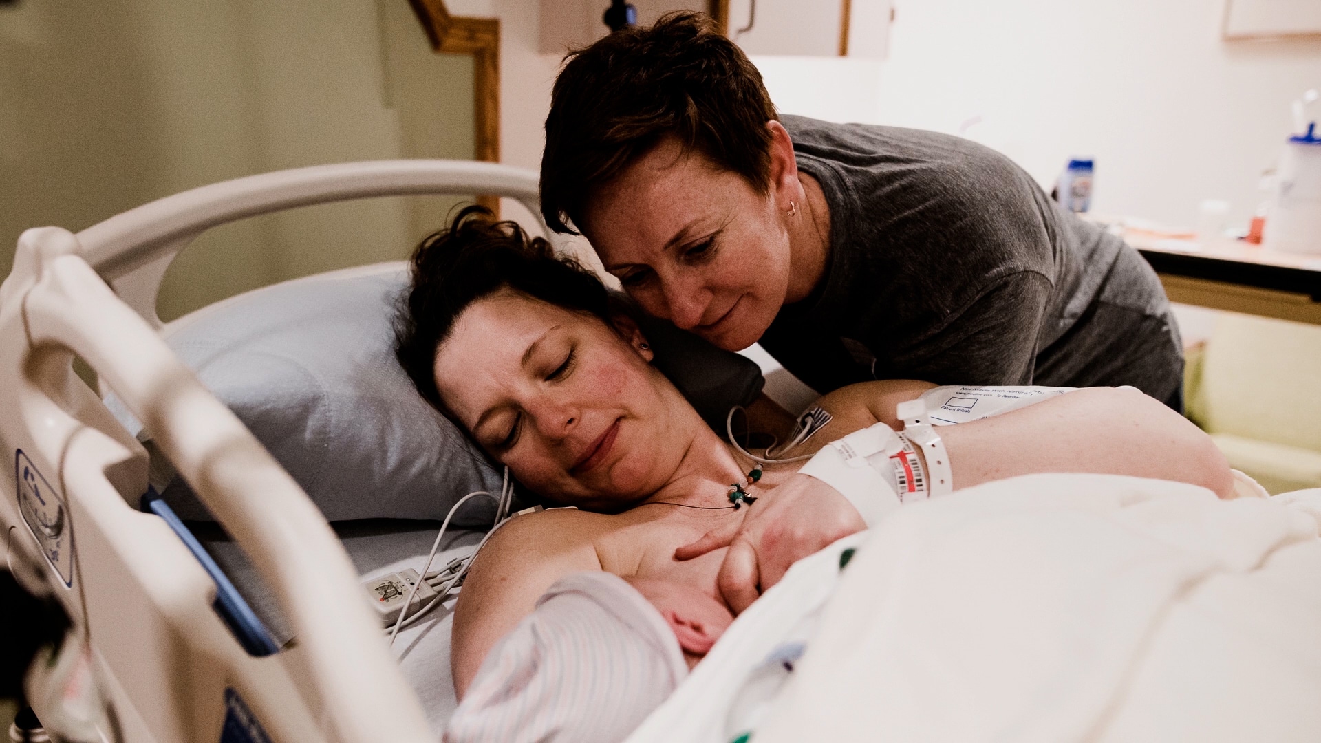 two moms looking at their newborn baby in the hospital