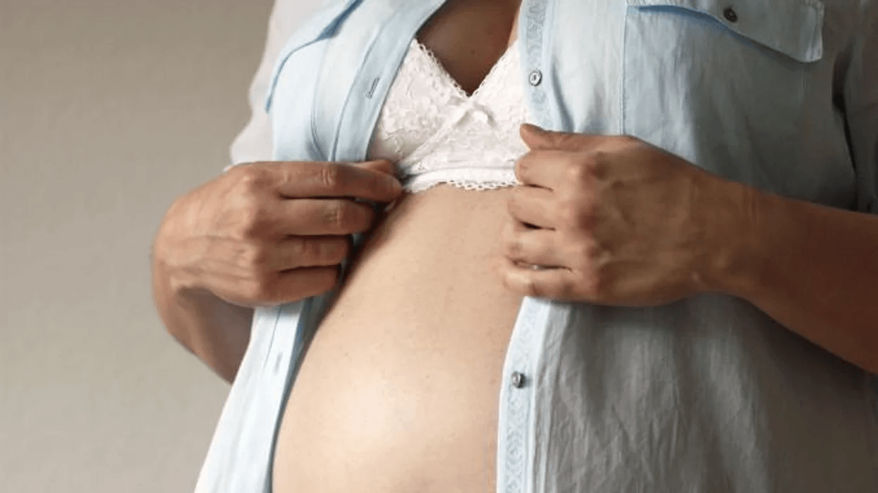 pregnant woman opening shirt to reveal pregnant belly