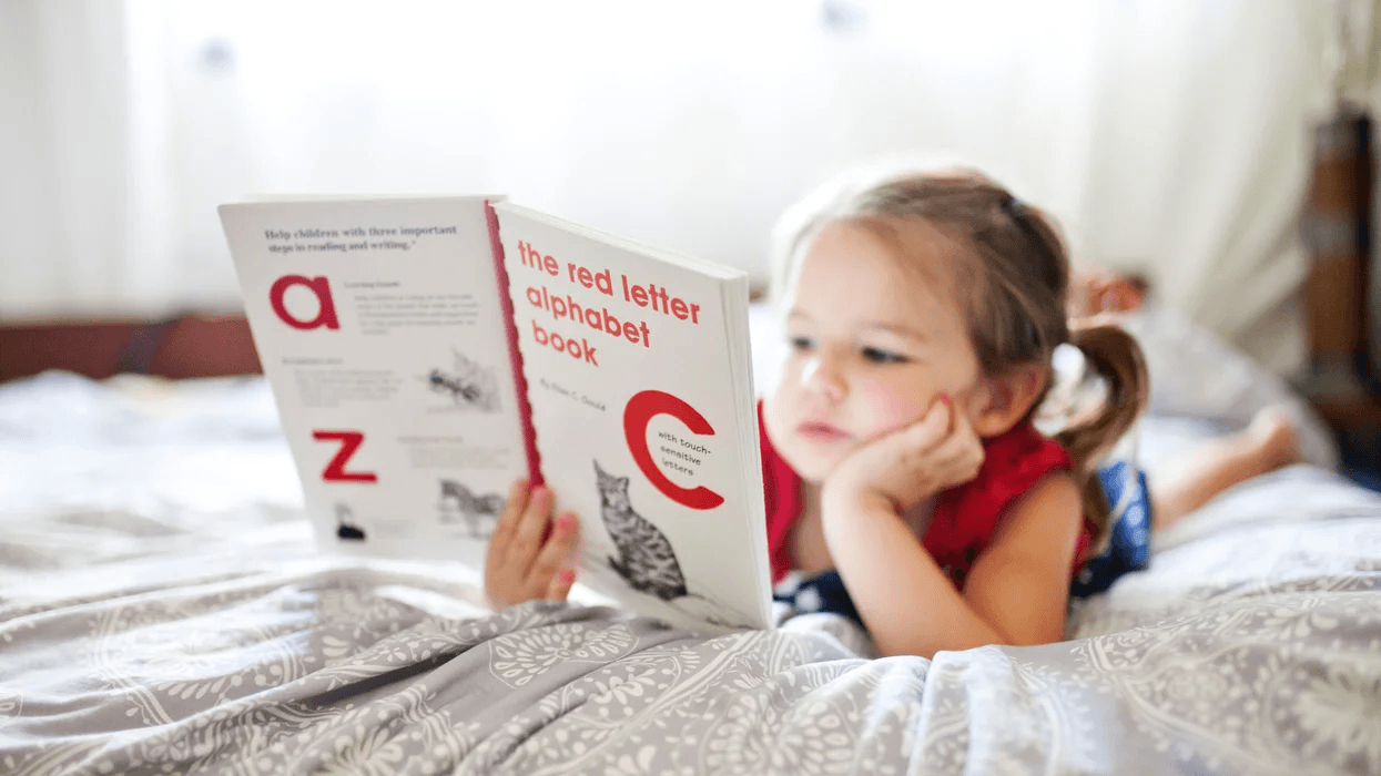 little girl reading a book in bed