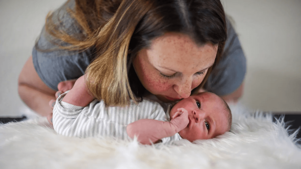 mom leaning over to kiss newborn baby