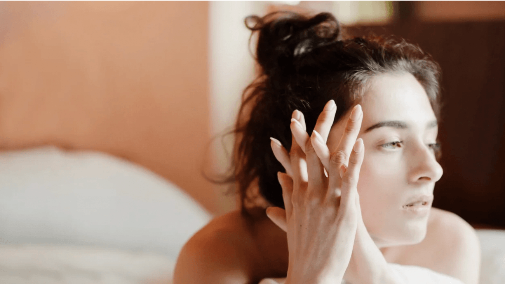 woman on bed with hands on head thinking