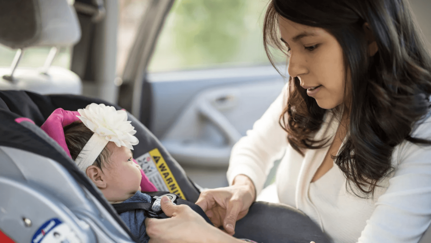 mom helping baby in a car sear