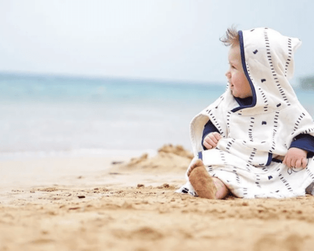 baby sitting on a beach wrapped in a towel