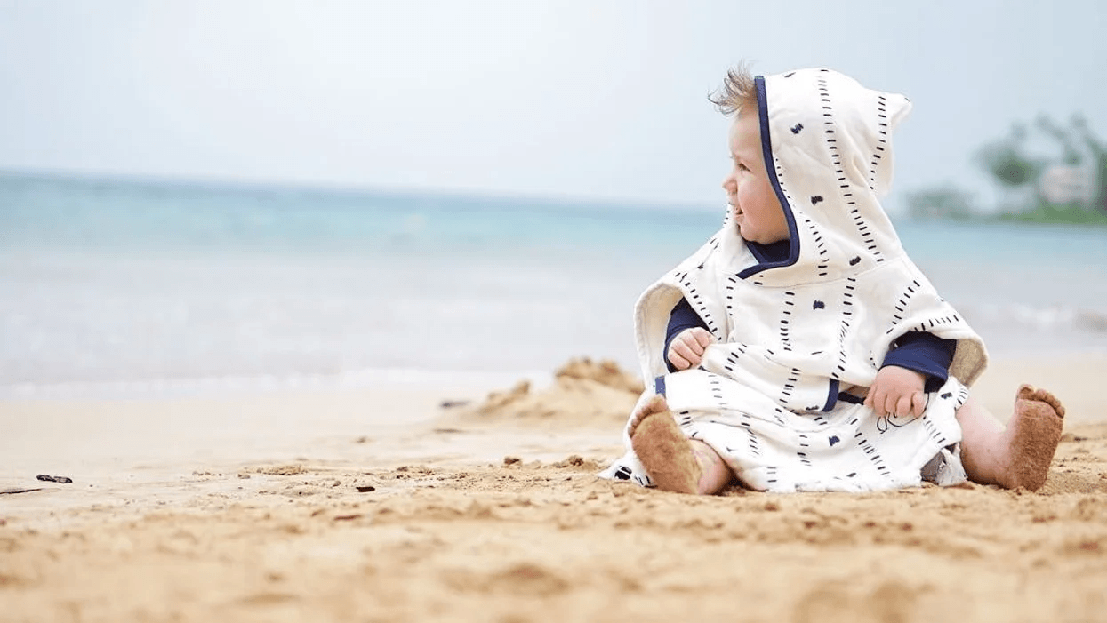 baby sitting on a beach wrapped in a towel