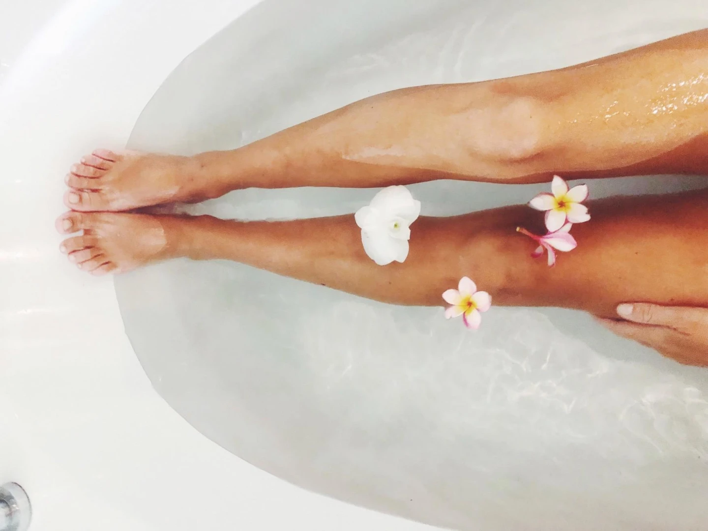 woman's legs in bathtub with floating flowers