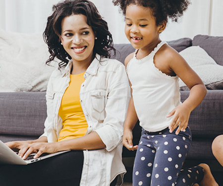 mom working on a laptop while her daughter plays behind her