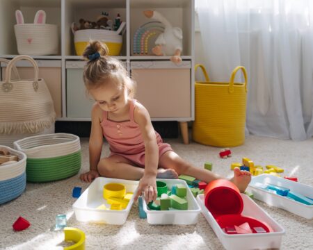 A Little Girl Playing With Colorful Wooden Blocks On Floor