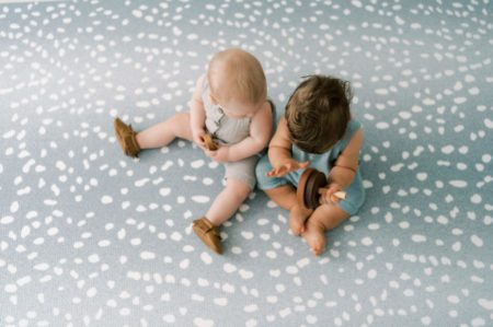 two babies playing on blue polka dot mat