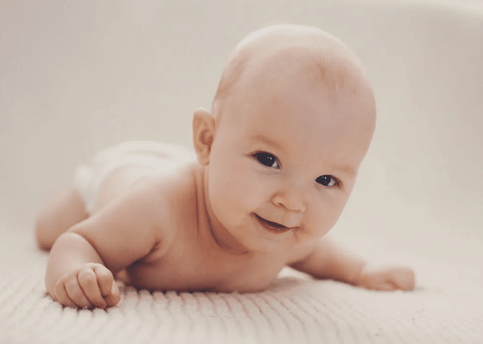 happy bald baby doing tummy time - 4 month milestones