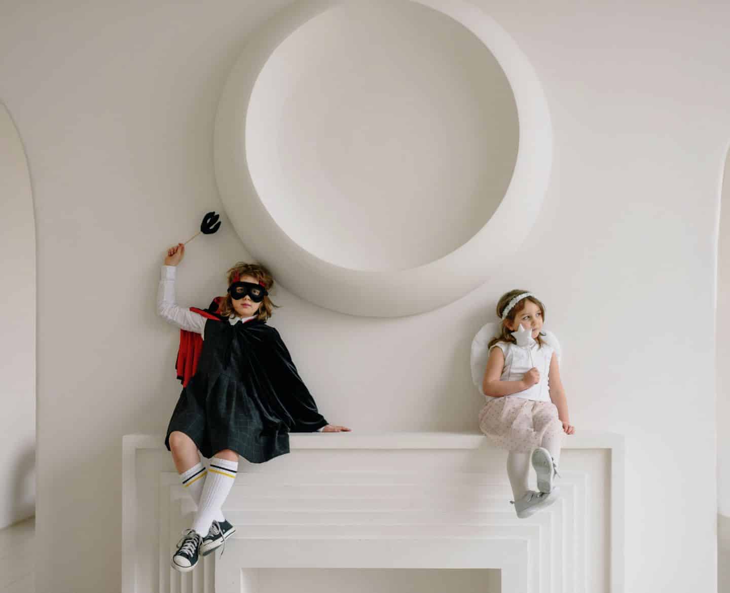 Two kids in Halloween costumes sitting on a mantle